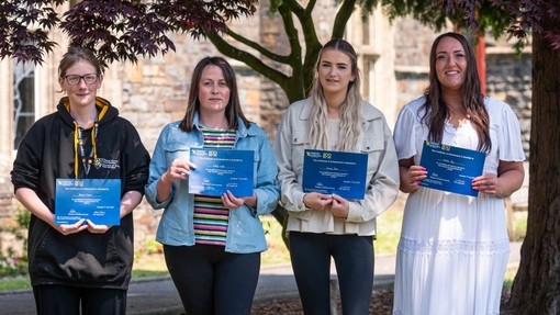 Four students stand in a line, holding certificates and smiling.