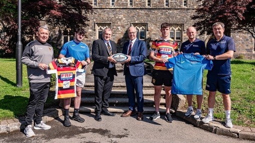 Cynrychiolwyr yr Academi Chwaraeon a Chlwb Rygbi Pêl-droed Quins Caerfyrddin yn dal crysau wedi’u brandio a phelen rygbi i fyny.
