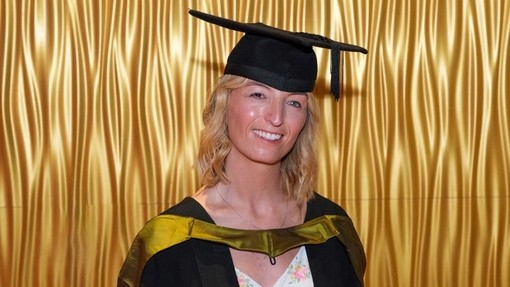 Carly Evans yn gwenu yn ei gynau graddio.