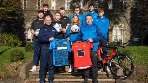 Myfyrwyr a staff yn sefyll yn dal cit chwaraeon y tu allan i’r Hen Adeilad, Caerfyrddin.
