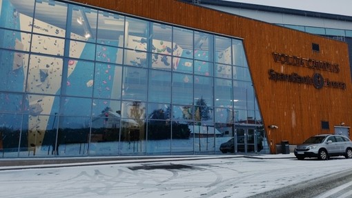Y tu allan i adeilad Coleg Prifysgol Volda yn Norwy; trwy’r ffasâd gwydr mae wal ddringo i’w gweld.