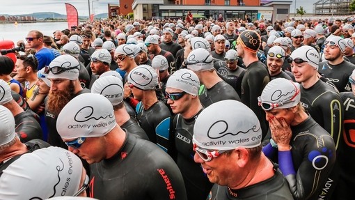 Athletwyr triathlon yn paratoi i blymio i’r dŵr yn SA1 Glannau Abertawe ar ddechrau cymal nofio’r gystadleuaeth.