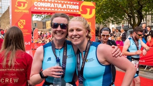 Dau athletwr triathlon blinedig ond hapus newydd orffen y ras yn Sgwâr y Castell Abertawe ac yn gwisgo eu medalau gyda balchder.