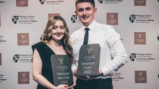 Carys Webster (Gweinydd Buddugol) a Sam Everton (Cogydd Buddugol) yn dal eu tabledi gwobr o lechfaen ac yn gwenu ar gyfer y camera.