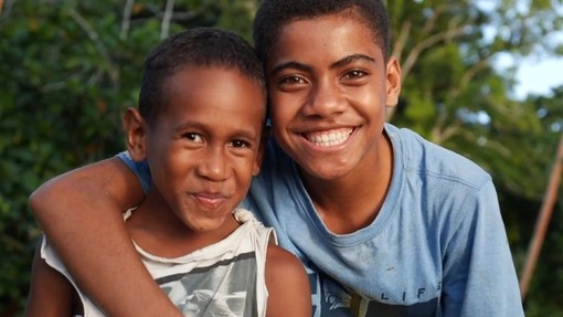 A Fijian boy grins into the camera with his arm around another boy's shoulders.