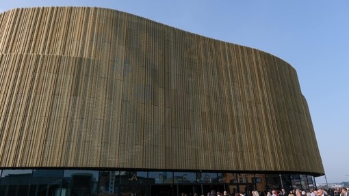 Ochr allanol Arena Abertawe wedi’i gorchuddio â phlatiau aur rhychiog.