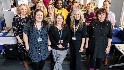 Un ar ddeg o staff PCYDDS yn gwenu o flaen coridor llydan yn llawn stondinau sy’n ymwneud â gyrfaoedd.