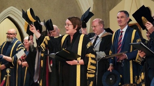Yn sefyll o flaen uwch aelodau eraill PCYDDS, mae’r Is-Ganghellor Elwen Evans yn diosg ei chap yn ystod y seremoni raddio.