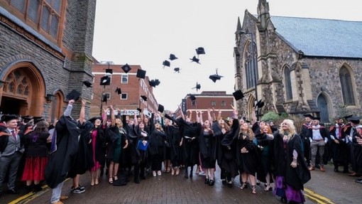 Mae myfyrwyr sy’n graddio yn taflu eu capiau academaidd yn yr awyr tu allan i Eglwys Caerdydd.