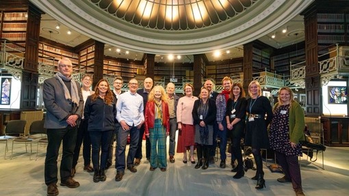 Crefftwyr proffesiynol a mynychwyr eraill y symposiwn yn gwenu dan gromen wydr yr ystafell ddarllen yng Ngholeg Celf Abertawe.