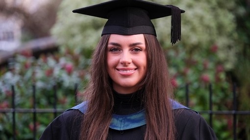 Fflur Davies yn gwenu yn ei gŵn a’i chap academaidd.