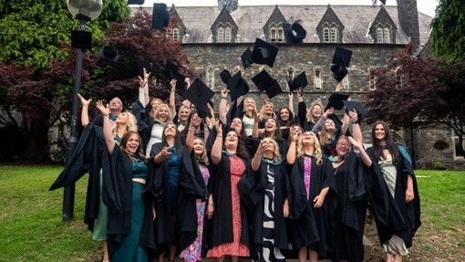 Graduating students throw their mortarboard hats in the air in front of the Old College, Carmarthen.