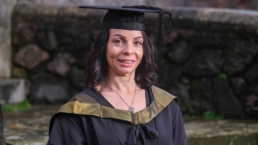 Emma Williams smiles slightly while wearing an academic hat and gown with a golden hood.