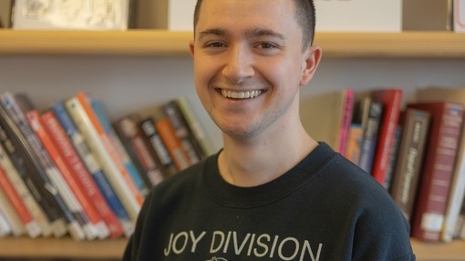 A smiling student wearing a black sweatshirt standing in front of a bookshelf full of books.