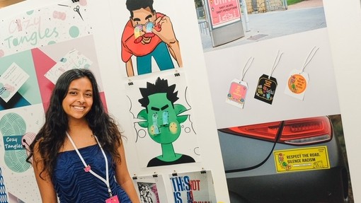 A smiling student standing in front of her colourful work.