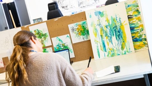 A student working at a desk surrounded by art work.