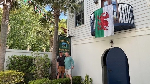 Dau ddyn yn sefyll o dan arwydd tafarn yn hongian o'r tŷ gyda baner. Mae'r arwydd yn dweud 'Y Ceffyl Du'