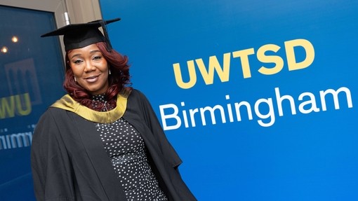 A smiling and proud Shana dressed in her graduation robes standing outside the EastSide Rooms.