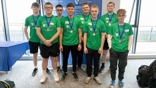 Wyth o fechgyn yn eu harddegau mewn crysau-t gwyrdd yn sefyll i gael tynnu llun grŵp, mae pob un yn gwisgo medal ar ruban las.