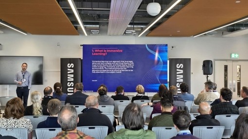 A seated audience listening to the presenter who is standing in front of a screen.
