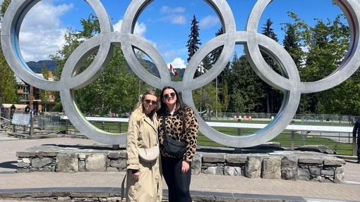 Two happy smiling girls standing in front of five interlinked steel rings.