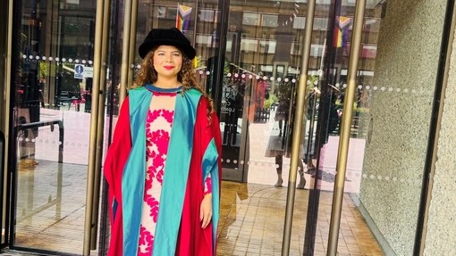 A happy, smiling graduate standing proudly, dressed in her cap and gown at graduation..