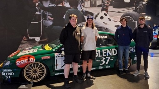 Students wearing casual clothing standing against a green racing car.