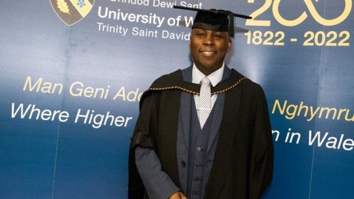 A smiling and proud Michael Thomas dressed in his cap and gown at his graduation ceremony.