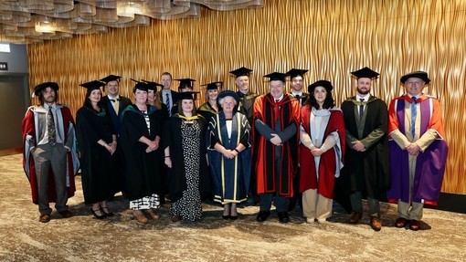A large group of lecturers and staff dressed in colourful caps and gowns.