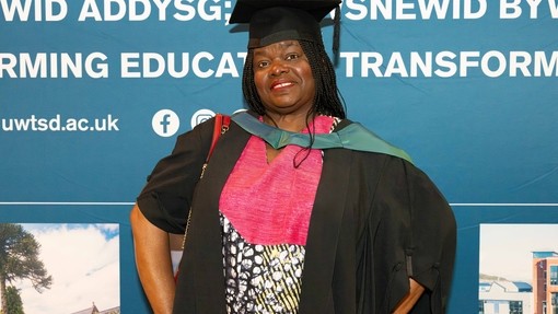 A happy, smiling graduate standing proudly, dressed in her cap and gown at graduation..