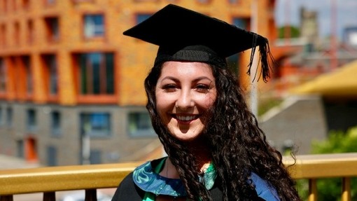 A smiling, happy graduate wearing her cap and gown.