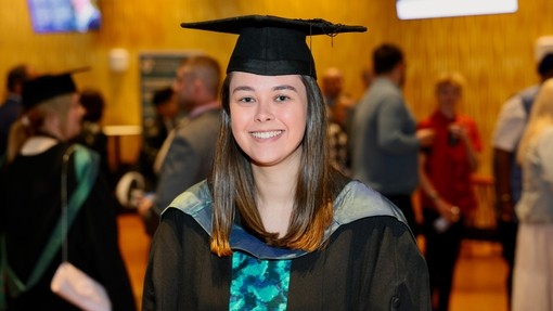 A happy, smiling graduate standing proudly, dressed in her cap and gown at graduation..