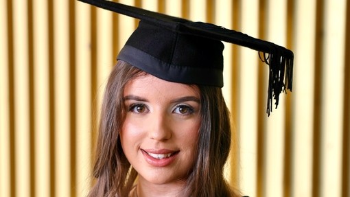 A happy, smiling graduate standing proudly, dressed in her cap and gown at graduation..