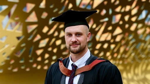 A happy, smiling graduate standing proudly, dressed in his cap and gown at graduation..