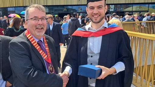 A happy, smiling graduate standing proudly, dressed in his cap and gown at graduation..