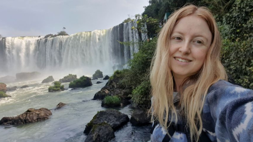 A smiling student dressed in outdoor wear, standing in front of a waterfall.