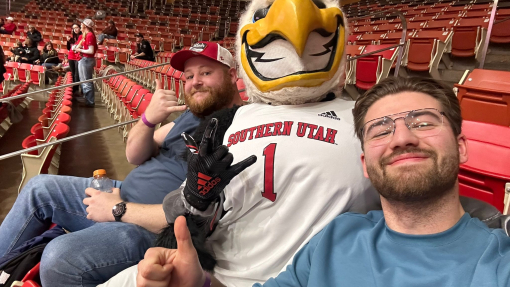 A photo of James Dillon sitting next door to a friend and somebody dressed up in an Eagle costume