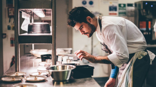 A man dressed in chef whites standing in a kitchen preparing food.