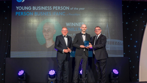 Three men on a stage. One is being handed an award by another man