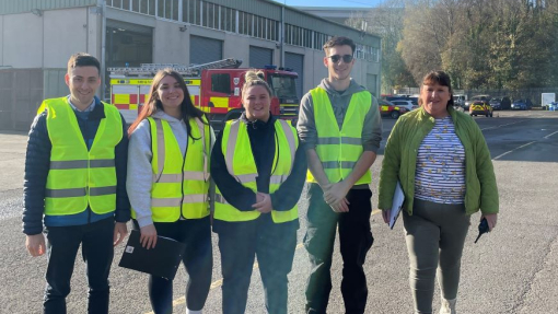 A group of people wearing high vis jackets standing in front of a fire engine at a training centre