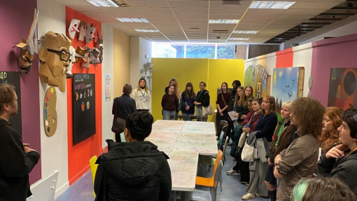 A group of students visiting an exhibition with art displayed on the walls.