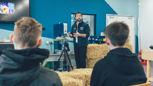 A lecturer standing in front of students in a lecture room with a bale of hay, demonstrating sustainable construction.