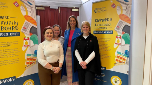 Four ladies standing in front of two large, colourful banners advertising the community cupboard.