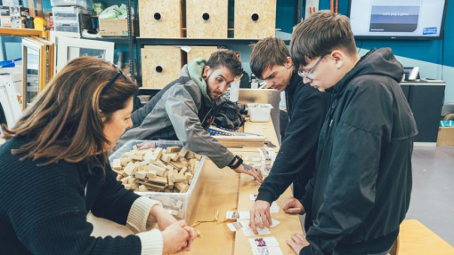 A group of students and lecturers standing around a wooden table with sustainable wood products.