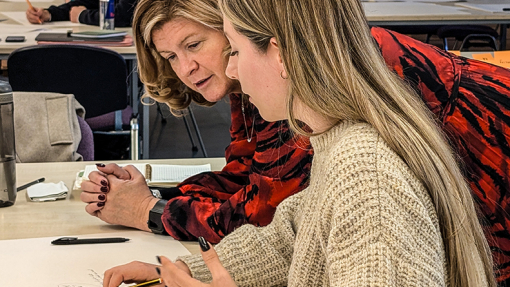 A female guest lecturer advising a student with work displayed on a white table.