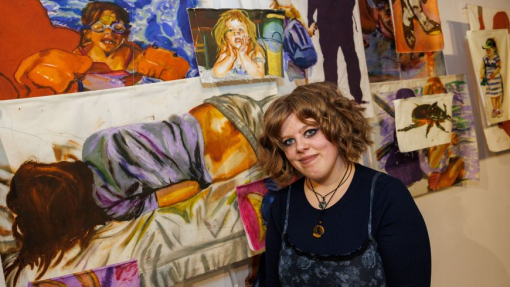 A student standing in front of several paintings at the exhibition.