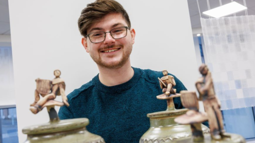 A happy smiling student showcasing his exhibition work of figures.