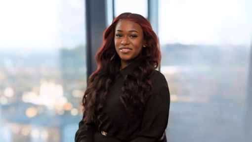 A smiling legal apprentice sitting in an office against a busy city background