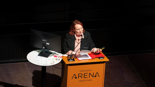 Jacqui Jones yn sefyll wrth ddarllenfa.