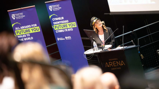 A smiling student with a pilot hat stands behind a podium in the packed auditorium.
